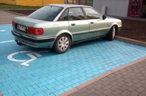 Samochód koloru jasnego zaparkowany na oznakowanym miejscu dla osób niepełnosprawnych