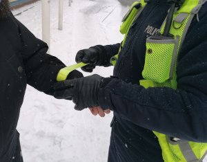 Zdjęcie przedstawia policjanta ruchu drogowego rozmawiającego z pieszym. Policjant zakłada na rękę pieszego opaskę odblaskową.