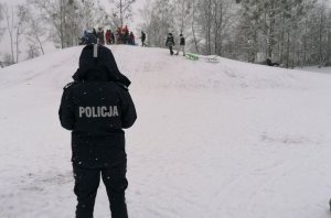 Zdjęcie przedstawia policjantkę stojącą na tle ośnieżonej górki w parku. Na górce znajdują się dzieci.