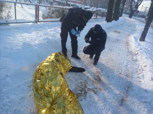 Zdjęcie przedstawia policjantów udzielających pomocy osobie potrzebującej. Osoba leży na chodniku, jest przykryta kocem termicznym. Na ziemi leży śnieg.