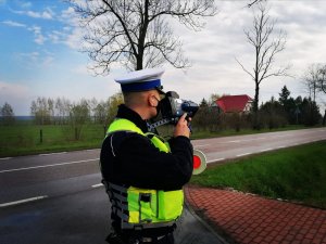 Zdjęcie przedstawia policjanta dokonującego pomiaru prędkości.